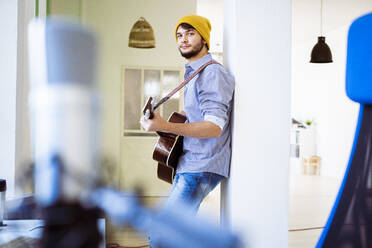 Confident guitarist playing guitar while leaning on pillar at studio - GIOF10206