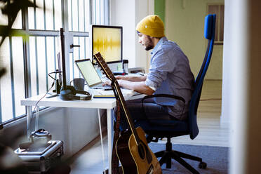Musiker arbeitet am Laptop, während er im Studio an der Gitarre sitzt - GIOF10210