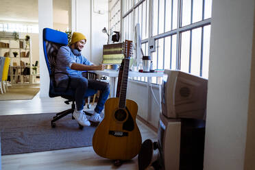 Smiling songwriter writing while sitting at desk in studio - GIOF10220