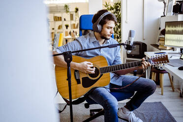 Gitarrist spielt Gitarre und sitzt am Mikrofonständer im Aufnahmestudio - GIOF10231