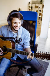 Lächelnder Musiker beim Aufnehmen von Musik und Gitarrenspiel im Tonstudio - GIOF10232