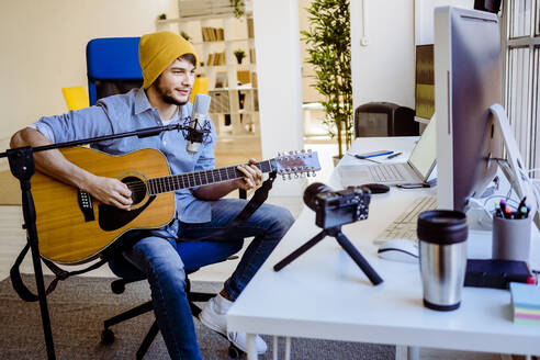 Musician teaching to play guitar on camera while sitting at recording studio - GIOF10236