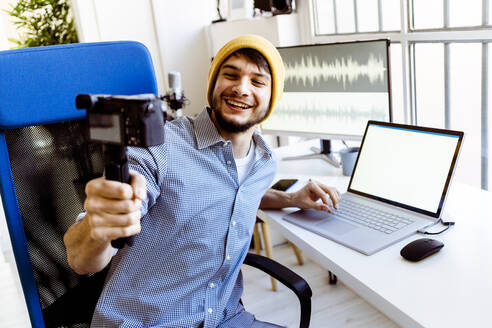 Smiling vlogger using laptop while recording on camera at studio - GIOF10240