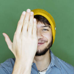 Lächelnder Mann, der sein Gesicht hinter der Hand versteckt, während er vor einem grünen Hintergrund steht - GIOF10250