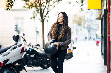 Young woman with helmet walking on sidewalk in city - JCMF01731