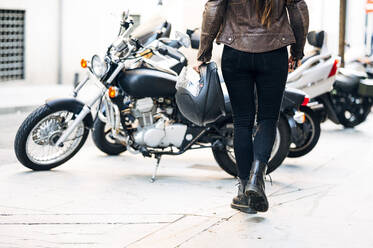 Motorradfahrerin mit Helm, die auf dem Bürgersteig in der Stadt auf ein Motorrad zugeht - JCMF01732