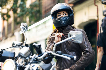 Bikerin mit Helm und Lederjacke, die in der Stadt wegschaut - JCMF01734