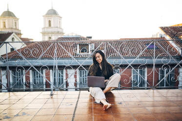 Young woman using laptop while sitting on terrace against clear sky - JCMF01746