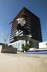 Man practicing kickflip with skateboard while jumping at skateboard park - PNAF00378