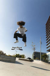 Junger Sportler übt Kickflip mit Skateboard an einem sonnigen Tag - PNAF00379