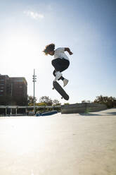 Lockenkopf Mann macht Kickflip mit Skateboard an sonnigem Tag - PNAF00380