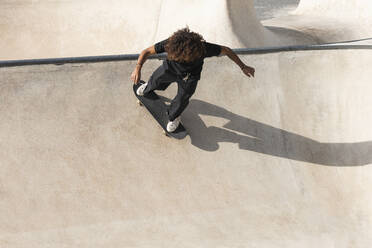 Curly hair sportsman practicing skateboarding on sports ramp at skateboard park - PNAF00397