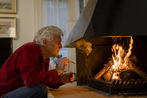 Mann raucht Zigarette, während er zu Hause am Kamin sitzt - AFVF07919