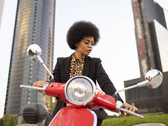 Von unten selbstbewusste afroamerikanische Frau mit Motorrad in schwarzer klassischer Kleidung schaut nach unten - ADSF19608