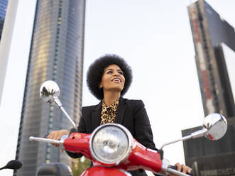 Von unten fröhliche afroamerikanische Frau mit Motorrad in schwarzem klassischen Outfit, die wegschaut - ADSF19609