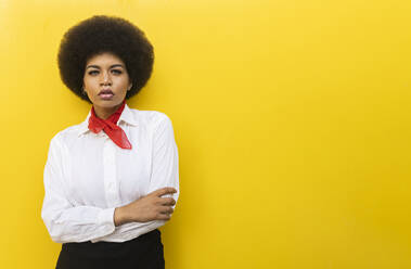 Selbstbewusste afroamerikanische Frau in elegantem formellen Outfit, stehend mit verschränkten Armen vor gelbem Hintergrund - ADSF19610