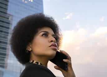 Von unten Seitenansicht einer afroamerikanischen Frau mit lockigem Haar, die auf der Straße steht und mit ihrem Smartphone telefoniert - ADSF19622