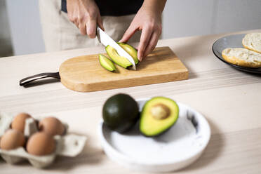 Hände einer Frau schneiden Avocado auf Schneidebrett - GIOF10336