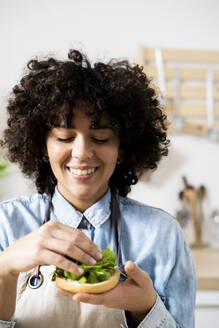 Portrait of young woman smiling while preparing vegan sandwiches with arugula - GIOF10343