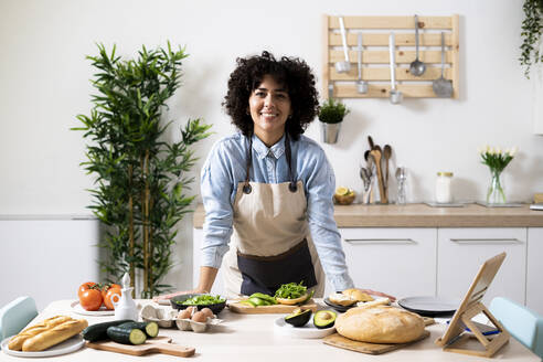 Porträt einer jungen Frau, die sich auf den Küchentisch stützt und in die Kamera lächelt - GIOF10346
