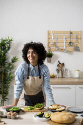 Porträt einer jungen Frau, die sich auf den Küchentisch stützt und wegschaut - GIOF10347