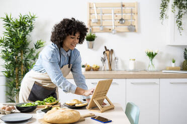 Young woman using digital tablet while preparing vegan sandwiches in kitchen - GIOF10352