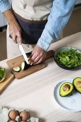 Mid section of woman slicing cucumber on cutting board - GIOF10353