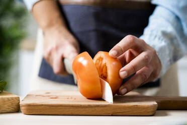 Die Hände einer Frau, die eine Tomate auf einem Schneidebrett schneidet - GIOF10356
