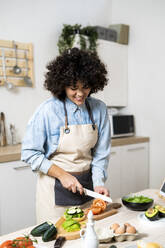 Portrait of young woman cutting vegetables in kitchen - GIOF10357