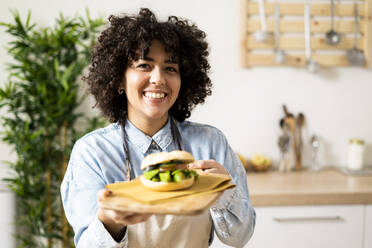 Porträt einer jungen Frau mit einem frisch zubereiteten veganen Sandwich - GIOF10362