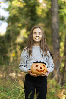 Smiling girl holding Halloween pumpkin while standing at park - XCF00304