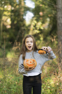 Mädchen mit offenem Mund steht mit Halloween-Kürbis im Park - XCF00306