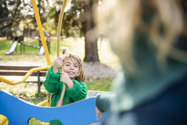 Lächelndes Mädchen zieht am Seil, während es mit seiner Mutter im Park spielt - MCVF00692