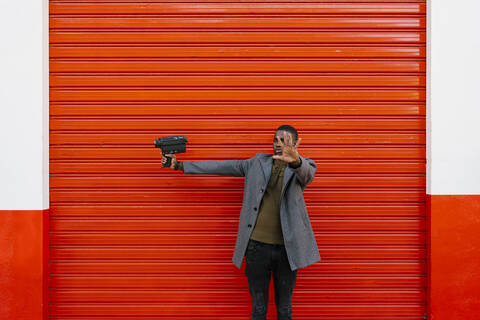 Man with old film camera showing stop gesture while standing against red wall stock photo