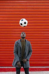 Junger Mann spielt mit Fußball, während er an einer roten Wand steht - EGAF01325