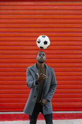 Mann spielt mit Fußball, während er an einer roten Wand steht - EGAF01326