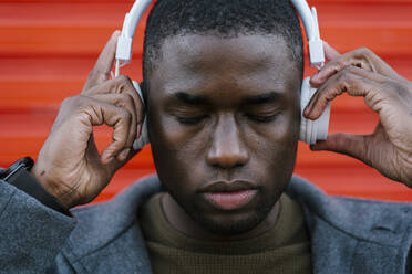 Mann hört Musik über Kopfhörer, während er an einer roten Wand steht - EGAF01336