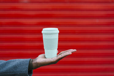 Man holding disposable coffee cup against red wall - EGAF01339