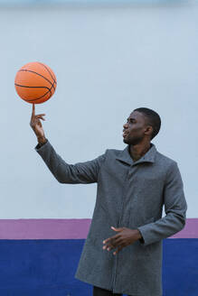 Mann dreht Basketball auf dem Finger, während er gegen eine mehrfarbige Wand steht - EGAF01343