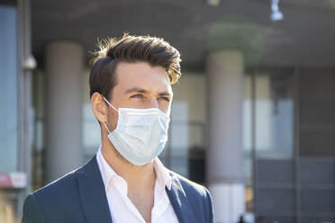 Close-up of businessman wearing face mask looking away against building - IFRF00230