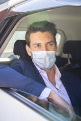Businessman wearing face mask looking through window while sitting in taxi - IFRF00231