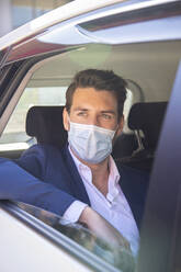 Close-up of businessman wearing face mask looking through window while sitting in taxi - IFRF00232