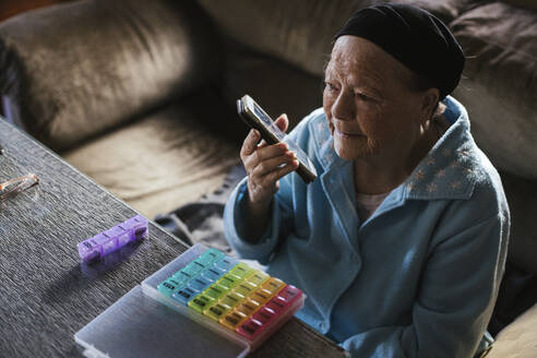 Ältere Frau, die eine Sprachnachricht über ein Mobiltelefon im Wohnzimmer sendet - LJF02021