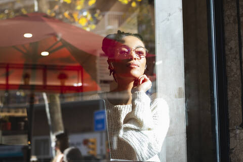 Selbstbewusste junge Frau mit Brille schaut durch das Fenster eines Cafés, lizenzfreies Stockfoto