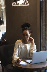 Beautiful young woman writing in diary while sitting with laptop at cafe - PNAF00410