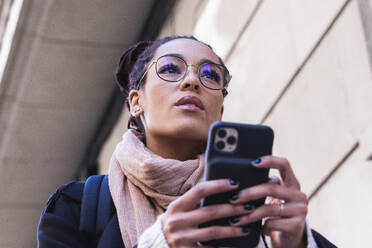 Schöne junge Frau schaut weg, während sie ein Smartphone hält - PNAF00440