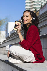 Smiling young female millennial sitting cross-legged with reusable coffee cup on sunny day - PNAF00445