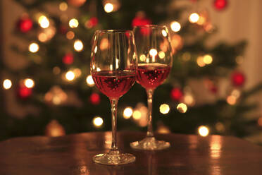 Rosenwein in glänzenden Weingläsern vor dem Weihnachtsbaum - JTF01754