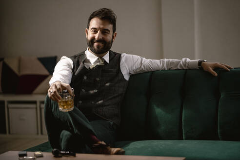 Porträt eines bärtigen Mannes auf dem Sofa mit einem Glas Whiskey in der Hand - GIOF10375