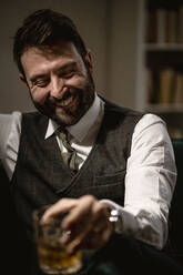 Portrait of bearded man laughing while enjoying glass of whiskey - GIOF10377